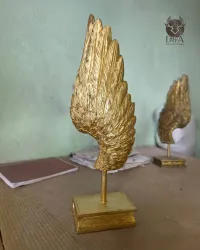 Escultura de alas de ángel doradas: estatua decorativa sobre una base con forma de libro.